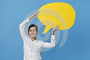 Happy brunette woman in elegant white shirt with yellow speech bubble on blue background