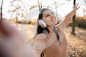 Happy brunette woman in headphones listening to music and dancing in autumn in the park