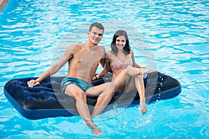 Happy brunette woman and the man having fun on a mattress at the swimming pool on their vacation