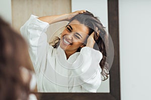 Happy brunette woman with palms in her hair looking at mirror reflection