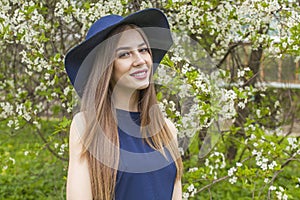 Happy brunette woman portrait. Beautiful female model with long hair and make-up wearing classic blue hat in spring garden outdoor