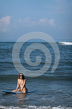 Happy brunette woman sitting on blue surfboard in the ocean. Surfer girl having fun inside ocean during the summer in holiday and