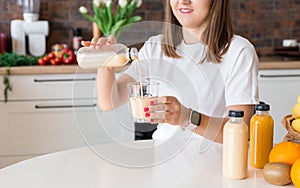 Happy brunette woman sitting with bottle of smoothie and fruits at home kitchen. Vegan meal and detox concept. Girl with