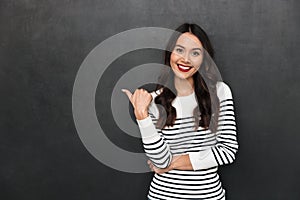 Happy brunette woman in sweater pointing away with thumb