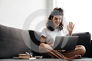 Happy brunette woman waving hand while taking video call on laptop