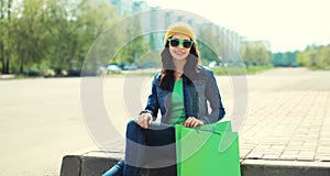 Happy brunette young woman with shopping bags sitting in the city