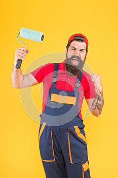 Happy brutal man in boilersuit uniform. mature hipster use paint roller tool for painting. repairman or builder working