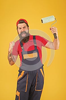 happy brutal man in boilersuit uniform. mature hipster use paint roller tool for painting. repairman or builder working