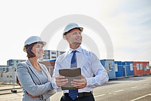 Happy builders in hardhats with tablet pc outdoors