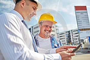 Happy builders in hardhats with tablet pc outdoors