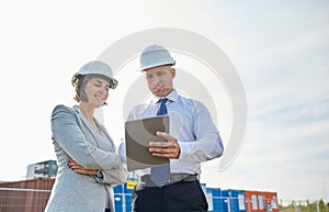 Happy builders in hardhats with tablet pc outdoors