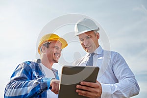 Happy builders in hardhats with tablet pc outdoors