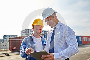 Happy builders in hardhats with tablet pc outdoors