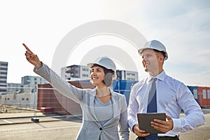 Happy builders in hardhats with tablet pc outdoors