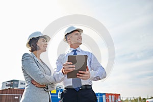 Happy builders in hardhats with tablet pc outdoors