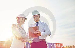 Happy builders in hardhats with tablet pc outdoors