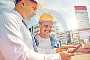 Happy builders in hardhats with tablet pc outdoors