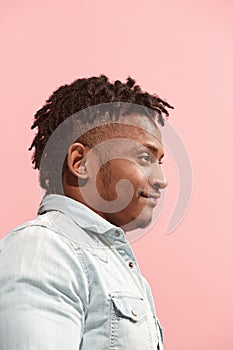 The happy business Afro-American man standing and smiling against pink background. Profile view.