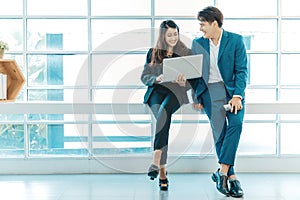 Happy business couple standing together  checking work on laptop near the window.