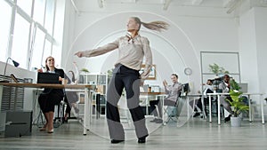 Happy business lady dancing in office celebrating success while staff clapping hands sitting at desks