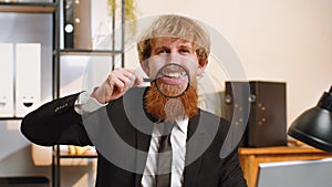 Happy business man holding magnifier glass on teeth, looking at camera, smiling silly face mouth