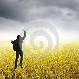 Happy business man jumping in yellow rice field and rainclouds photo