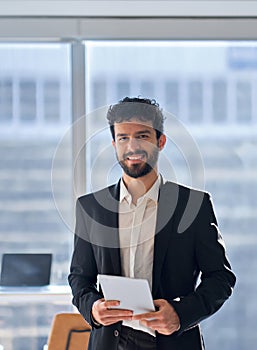 Happy business man standing in office holding tablet. Vertical portrait.