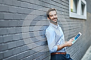 Happy business man, tablet and portrait on wall for web research, email or info online in city. Smile, digital tech and