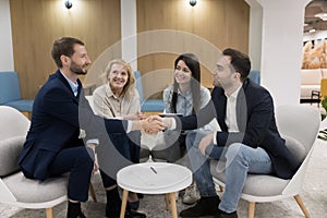 Happy business partners shake hands seated in modern office hallway