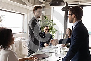 Happy business partners shaking hands at meeting, standing in boardroom