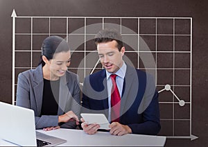 Happy business people at a desk looking at a tablet against brown background with graphic
