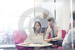 Happy business people discussing over laptop in office meeting