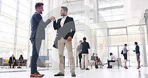 Happy business people, friends greeting with a fist bump in diverse corporate office. Businessmen greeting before