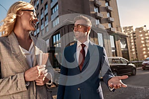 Happy business people. Two cheerful colleagues in classic wear talking about new project and smiling while walking