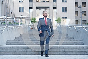 Happy business person walks downstairs in hurry movement with tablet. Young contemporary businessman walking in finance centre