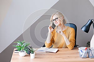 Happy business woman calling on mobile phone and making notes in notepad