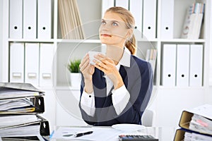 Happy business woman or female accountant having some minutes for coffee and pleasure at working place