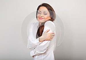 Happy business woman hugging herself with natural emotional enjoying face with closed eyes on blue background. Love concept