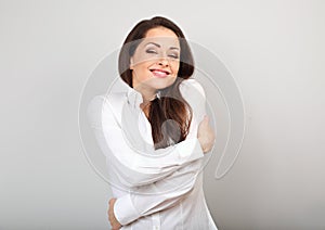 Happy business woman hugging herself with natural emotional enjoying face with closed eyes on blue background. Love concept