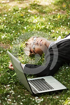 Happy business woman with laptop lying on the grass