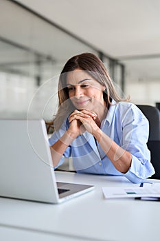 Happy business woman of middle age looking at laptop working in office. Vertical
