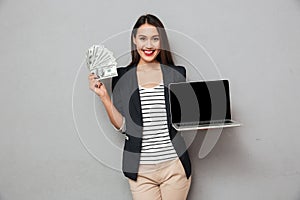 Happy business woman showing blank laptop computer and holding money