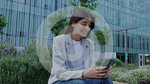 Happy business woman in smart casual using mobile phone over office buildings