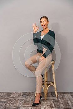 Happy business woman standing over grey wall background showing okay gesture.