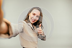 Happy business woman in suit makes selfie on beige background with smile on face and shows gesture like