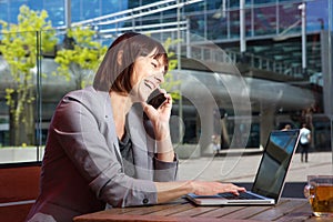 Happy business woman talking on mobile phone while working on laptop