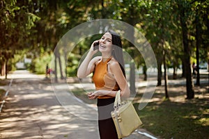 Happy business woman talking on the phone walking on the road in the park with bag