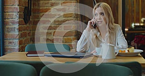 Happy business woman talking smartphone with in cafe. Cheerful woman talking on mobile phone with coworker in cafe.