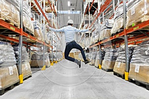 Happy businessman in helmet jumping at warehouse