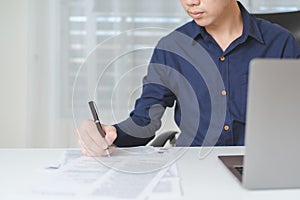 Happy businessman, male businessperson writing on paperwork with computer laptop on desk at office. Professional entrepreneur